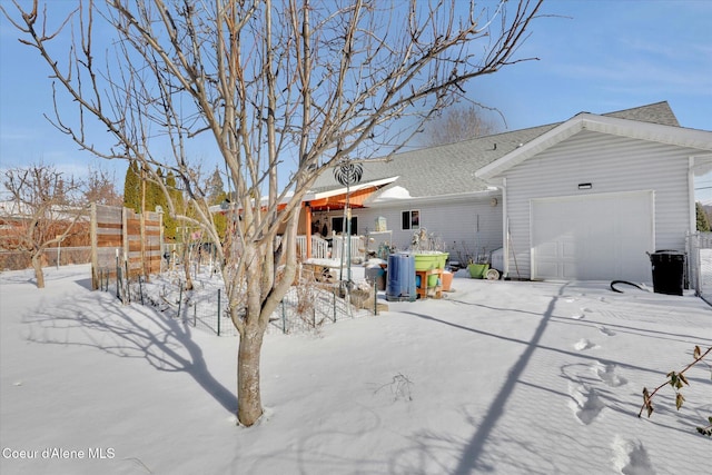 snow covered rear of property featuring an attached garage, fence, and roof with shingles