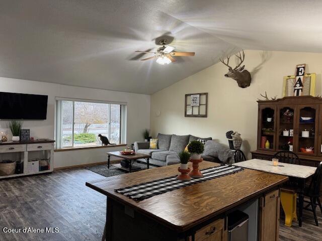 living area with dark wood-type flooring, lofted ceiling, ceiling fan, and baseboards