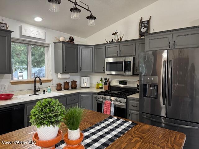 kitchen with gray cabinets, vaulted ceiling, stainless steel appliances, light countertops, and a sink