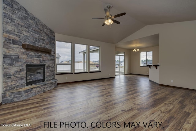 unfurnished living room featuring vaulted ceiling, a stone fireplace, wood finished floors, baseboards, and ceiling fan with notable chandelier