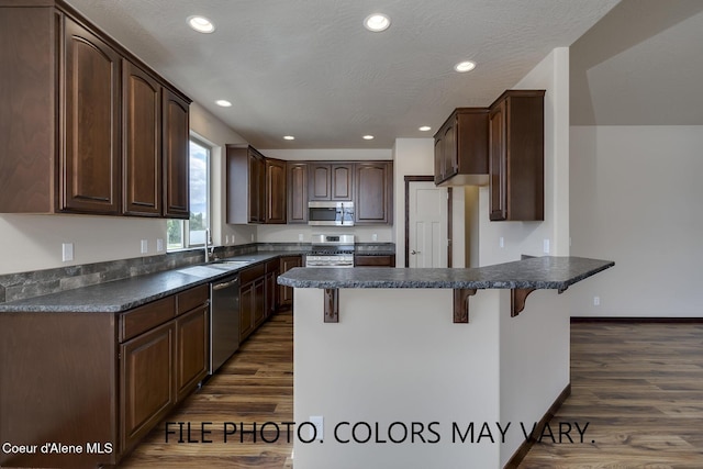 kitchen with a breakfast bar, dark wood-style flooring, stainless steel appliances, dark countertops, and a peninsula