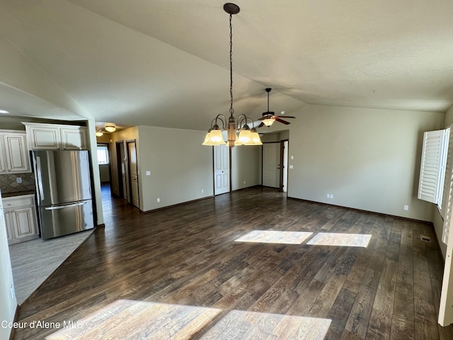 unfurnished dining area with dark wood finished floors, lofted ceiling, visible vents, baseboards, and ceiling fan with notable chandelier