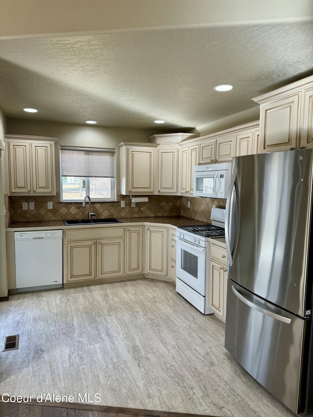 kitchen featuring white appliances, a sink, visible vents, cream cabinetry, and light wood finished floors