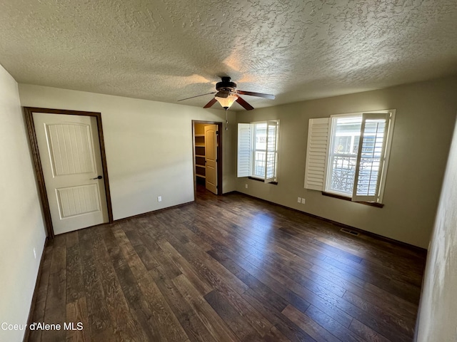 unfurnished bedroom featuring baseboards, visible vents, dark wood-style flooring, a walk in closet, and a textured ceiling