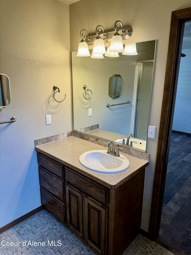 bathroom featuring a shower with shower door, vanity, and baseboards