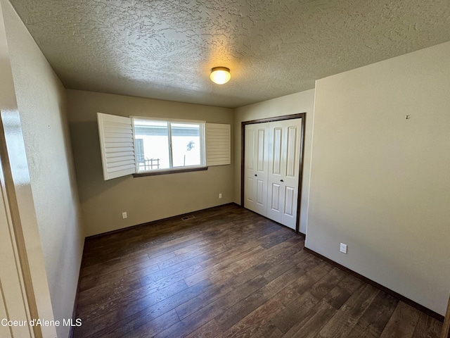 unfurnished bedroom with dark wood-style floors, a closet, a textured ceiling, and baseboards