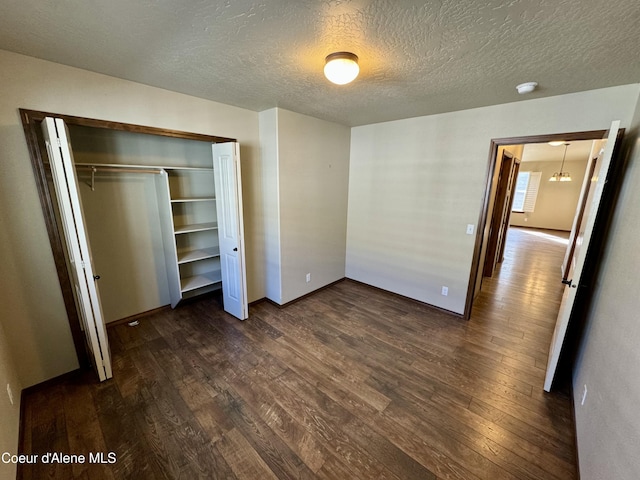 unfurnished bedroom with a textured ceiling, a closet, and dark wood-style flooring