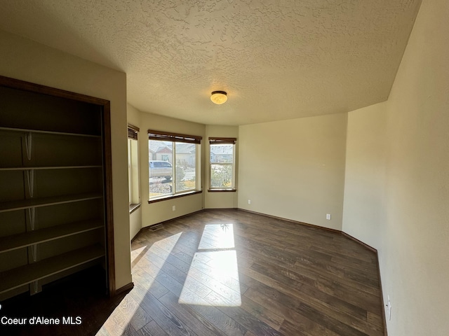 unfurnished bedroom with dark wood-type flooring, a textured ceiling, and baseboards