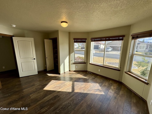 spare room with a textured ceiling, dark wood-type flooring, a wealth of natural light, and baseboards