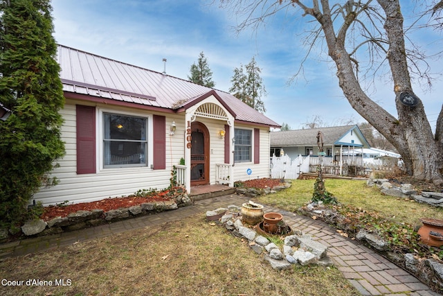 view of front facade with metal roof, a front lawn, and fence