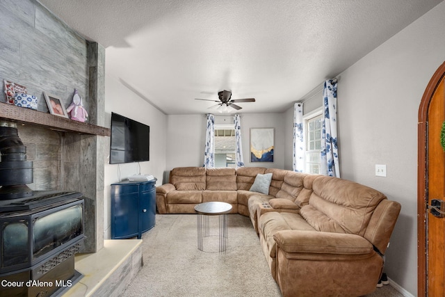 carpeted living area featuring a wood stove, ceiling fan, and a textured ceiling