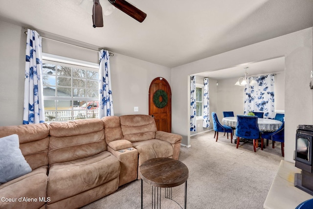 living room featuring carpet floors, a wood stove, and ceiling fan with notable chandelier