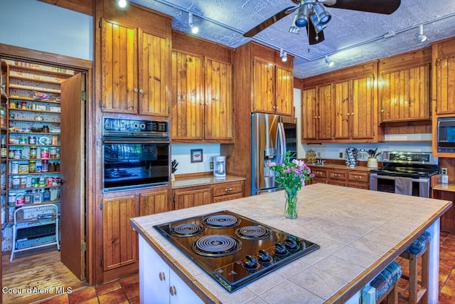 kitchen with a center island, brown cabinets, tile counters, ceiling fan, and black appliances