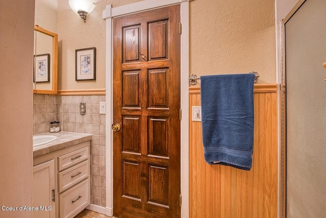 bathroom with tile walls, a wainscoted wall, a textured wall, and vanity