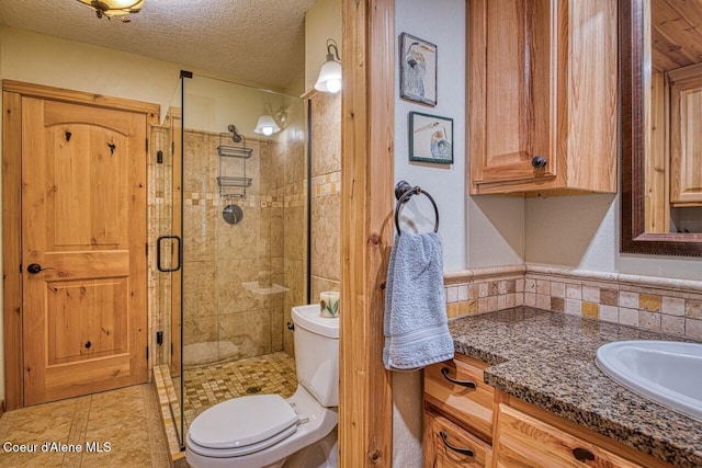 full bath with toilet, a shower stall, a textured ceiling, and vanity