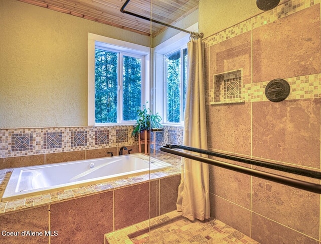 full bathroom featuring a textured wall, tiled shower, and a bath