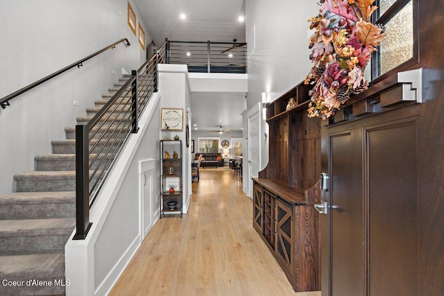 foyer entrance featuring a towering ceiling, ceiling fan, track lighting, light wood-type flooring, and stairs