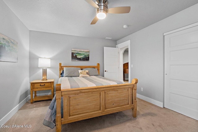 bedroom with light carpet, baseboards, arched walkways, ceiling fan, and a textured ceiling