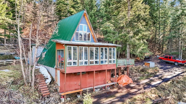 back of house featuring metal roof, a forest view, and a sunroom