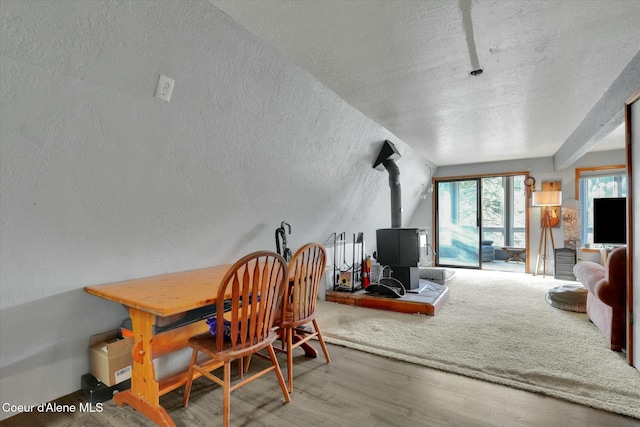 dining room featuring a wood stove, a textured ceiling, wood finished floors, and a textured wall