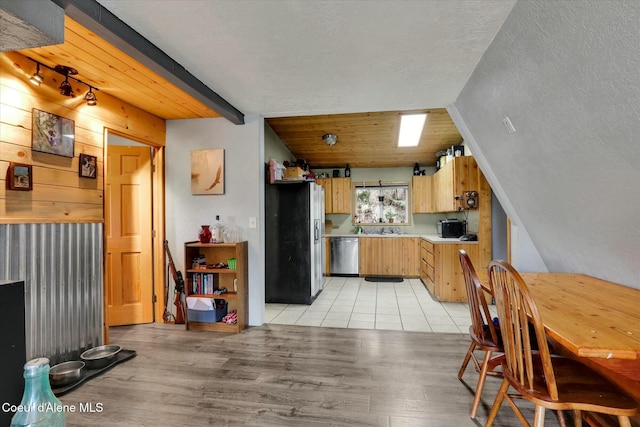 kitchen with vaulted ceiling with beams, stainless steel appliances, wood walls, light countertops, and light wood-type flooring