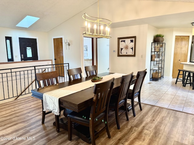 dining area featuring baseboards, lofted ceiling with skylight, an inviting chandelier, and light wood-style floors