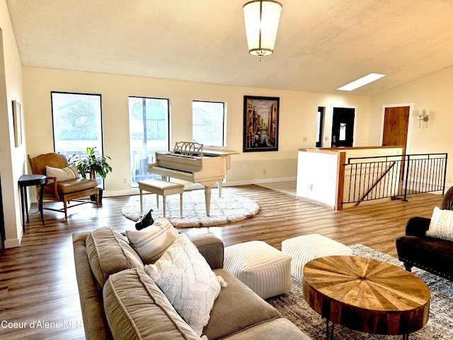 living area featuring vaulted ceiling with skylight, a textured ceiling, baseboards, and wood finished floors