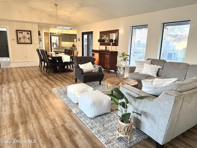 living room featuring vaulted ceiling, a textured ceiling, light wood-style flooring, and a notable chandelier