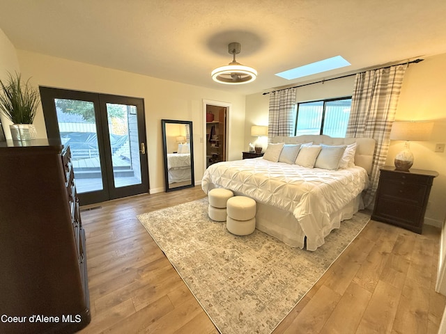 bedroom with access to exterior, light wood-type flooring, baseboards, and a skylight