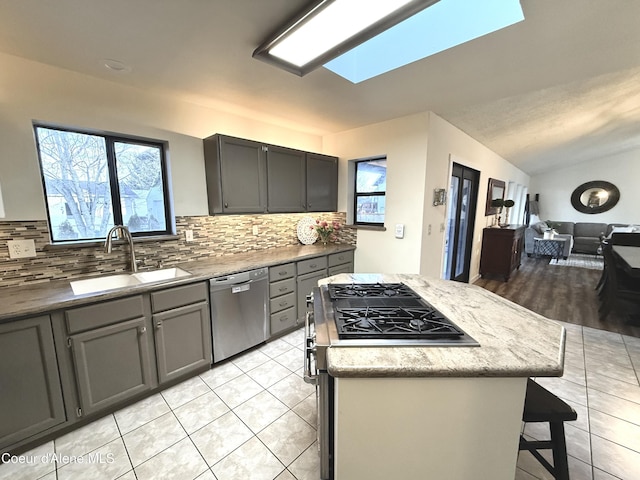 kitchen with light tile patterned flooring, a kitchen island, a sink, open floor plan, and appliances with stainless steel finishes