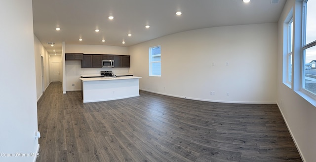 kitchen featuring baseboards, open floor plan, dark brown cabinets, stainless steel microwave, and dark wood finished floors