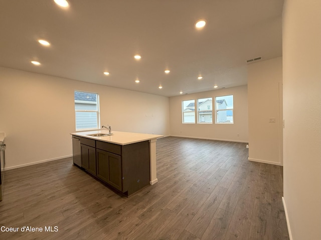 kitchen featuring a center island with sink, light countertops, visible vents, dark wood-type flooring, and a sink