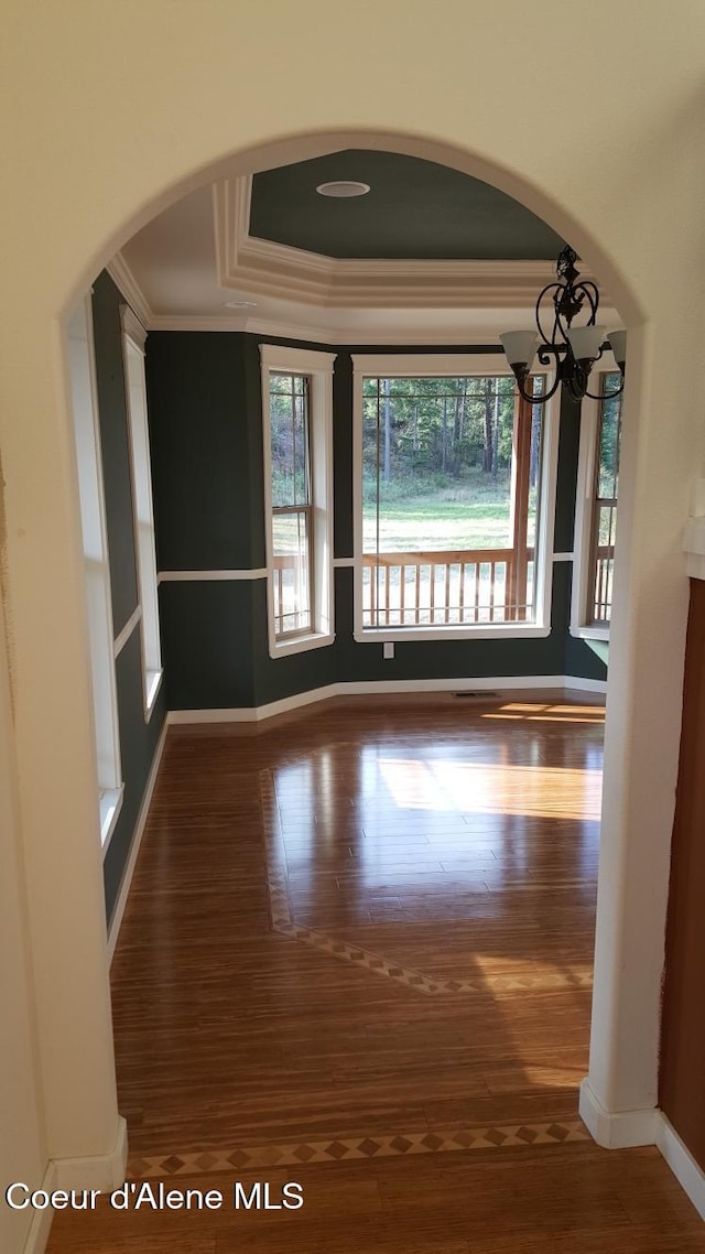 spare room featuring arched walkways, wood finished floors, baseboards, ornamental molding, and a tray ceiling