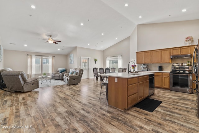 kitchen featuring a kitchen island with sink, a sink, open floor plan, light countertops, and stainless steel electric range oven