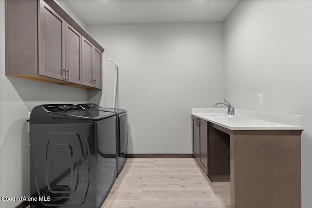 laundry area with cabinet space, baseboards, washing machine and clothes dryer, light wood-type flooring, and a sink