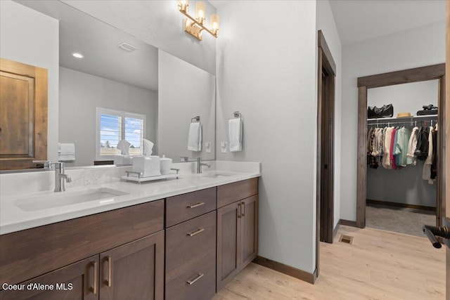 full bath featuring double vanity, visible vents, a sink, wood finished floors, and baseboards