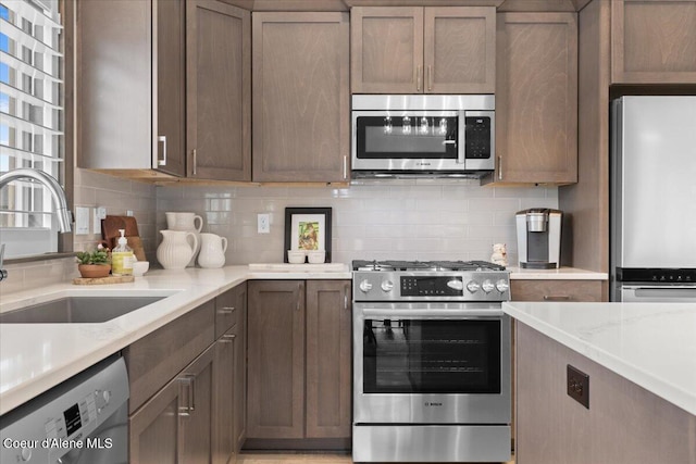 kitchen with appliances with stainless steel finishes, a sink, backsplash, and light stone counters