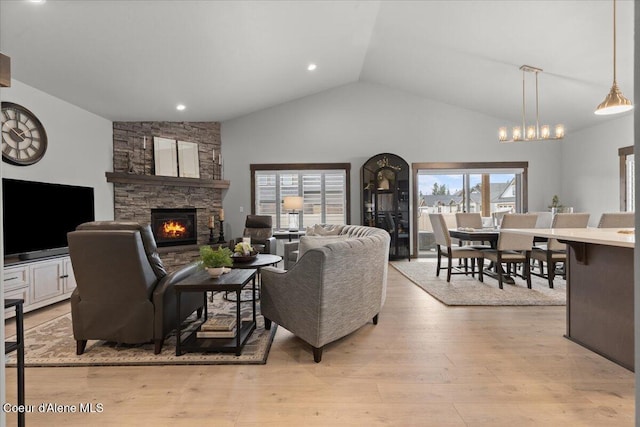 living room with high vaulted ceiling, a stone fireplace, and light wood-style floors