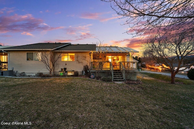 back of property at dusk featuring central AC, stairway, and a lawn