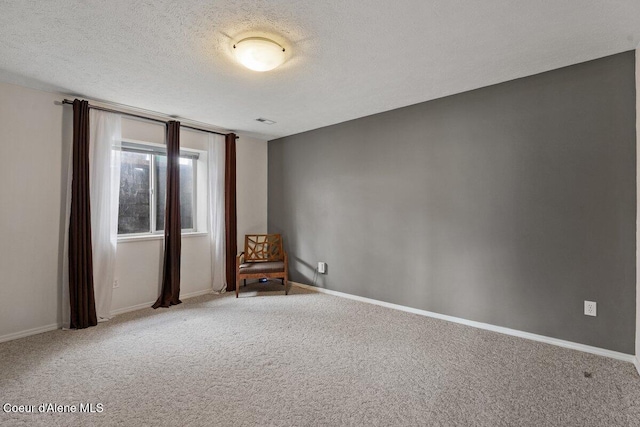 spare room with a textured ceiling, carpet floors, and baseboards