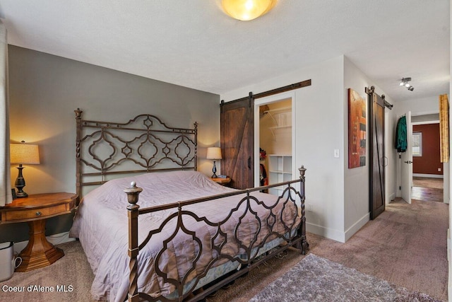 bedroom featuring a barn door, a spacious closet, baseboards, and carpet flooring