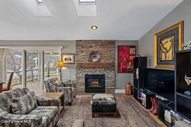 living room with a textured ceiling, a stone fireplace, and a skylight