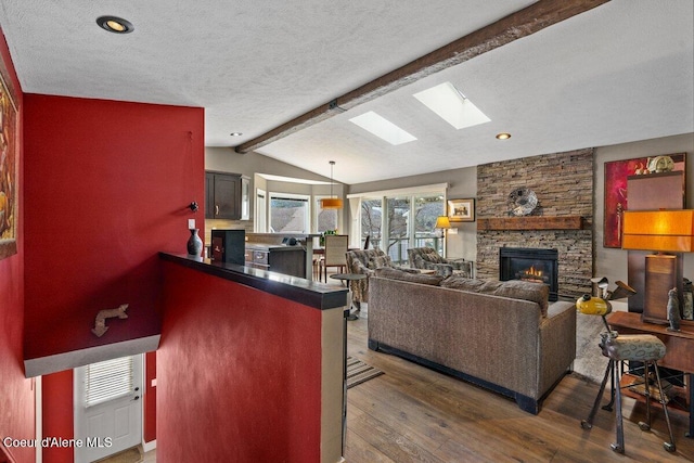 living area featuring vaulted ceiling with skylight, a stone fireplace, a textured ceiling, and hardwood / wood-style flooring