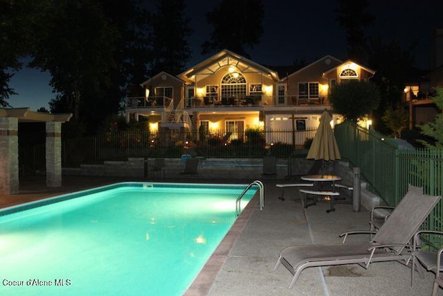 pool at night featuring fence, a fenced in pool, and a patio