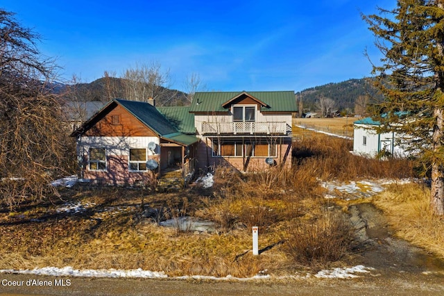 rear view of house with metal roof, a balcony, a chimney, and a mountain view