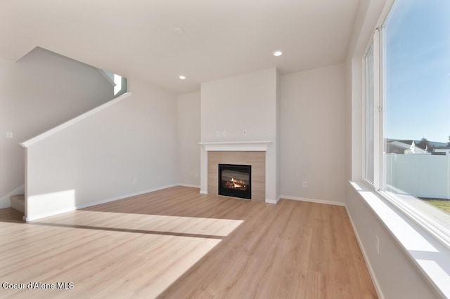 unfurnished living room featuring light wood finished floors, stairway, a tile fireplace, and baseboards