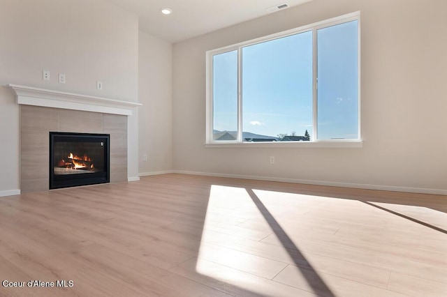 unfurnished living room featuring baseboards, a fireplace, visible vents, and wood finished floors