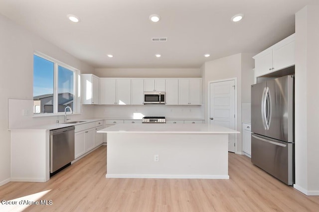 kitchen featuring white cabinets, a center island, light countertops, stainless steel appliances, and a sink