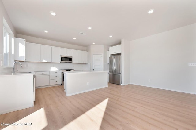 kitchen featuring a center island, stainless steel appliances, light wood-style flooring, decorative backsplash, and a sink