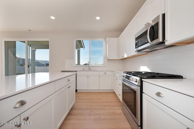 kitchen with white cabinets, a sink, stainless steel appliances, light countertops, and backsplash